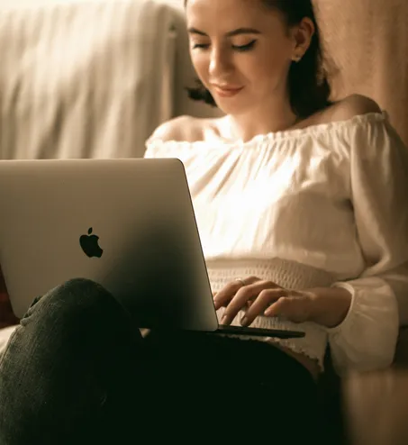 woman in white long sleeve shirt and black pants sitting on bed using macbook